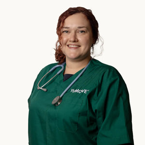 A smiling woman with red hair wearing green medical scrubs with a stethoscope around her neck, shown against a plain light background. The scrubs have the brand name YUMOVE printed on the chest.